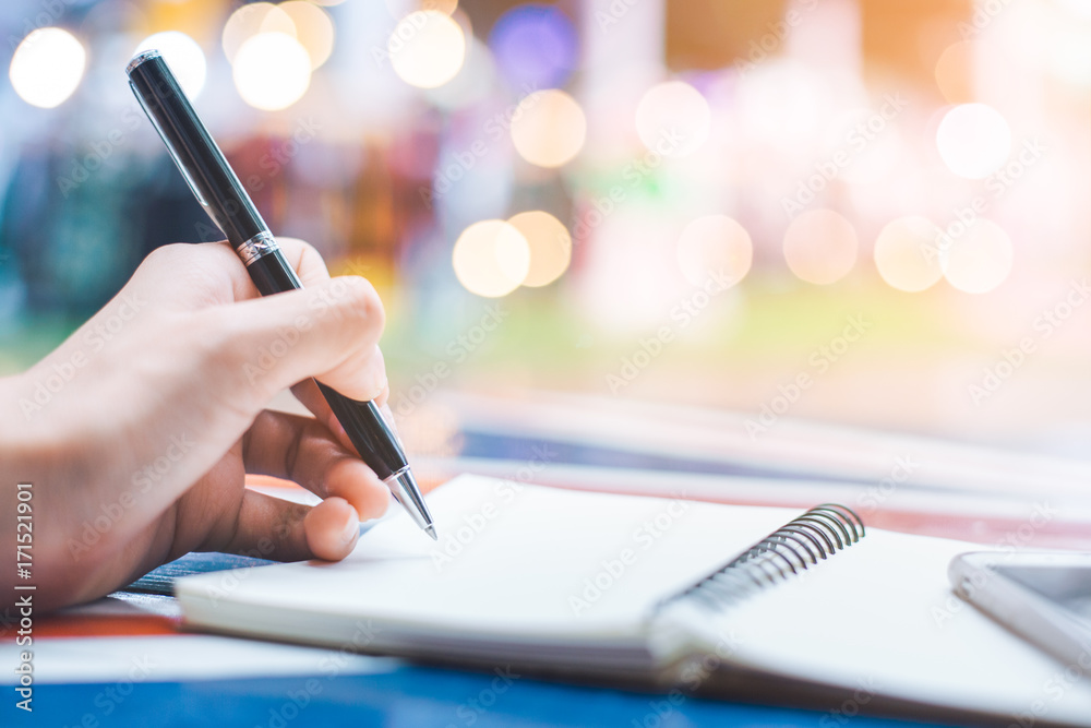 Woman's hand writing on a notebook with a pen on a wooden desk.Background blur backlight