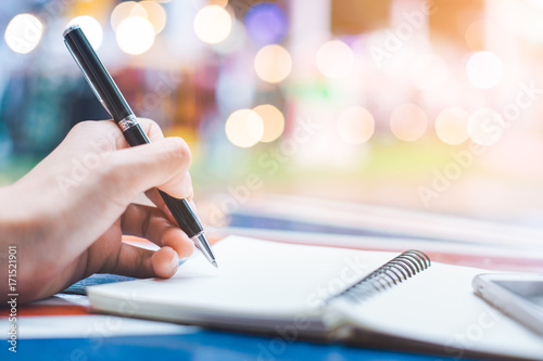 Obraz na płótnie Woman's hand writing on a notebook with a pen on a wooden desk.Background blur backlight w salonie