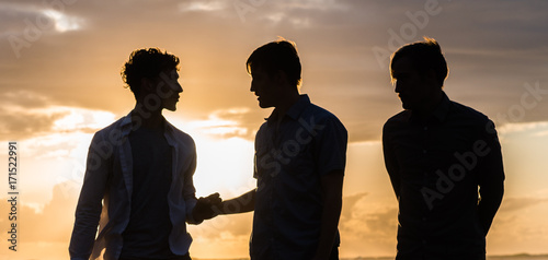 Tablou pe pânză Silhouette of three young men at the beach at sunset