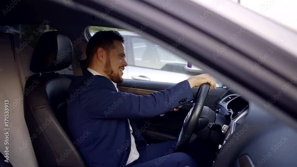 A young manager who is sitting in the car chatting with a friend on the smartphone and laughing loudly A young manager who is sitting in the car chatting with a friend on the smartphone and laughing loudly