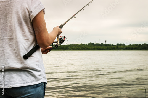 hands holding a fishing rod and twist the handle of the fishing reel. Shallow depth of field, soft focus