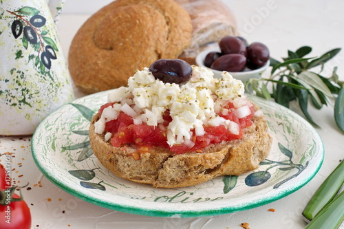Dakos traditional greek appetizer on a traditional plate with ceramic olive oil jar, dry rye bread, olives and olive branch. Healthy eating concept. Mediterranian lifestyle