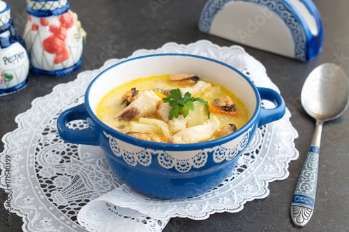 Creamy soup with fish fillet and mussels in a blue ceramic pot on a white cloth on a grey abstract background. Healthy eating concept. Meditteranian lifestyle