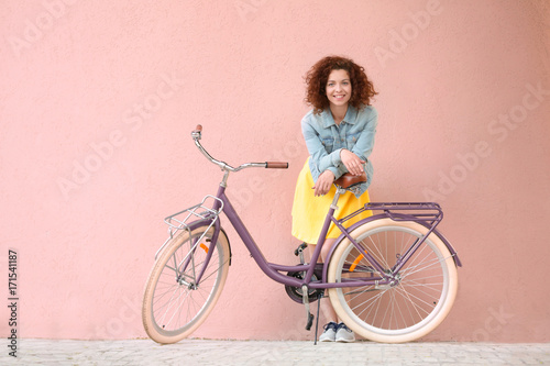 Fototapeta Naklejka Na Ścianę i Meble -  Beautiful young woman with bicycle on color wall background
