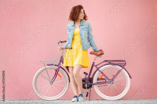 Beautiful young woman with bicycle on color wall background © Africa Studio