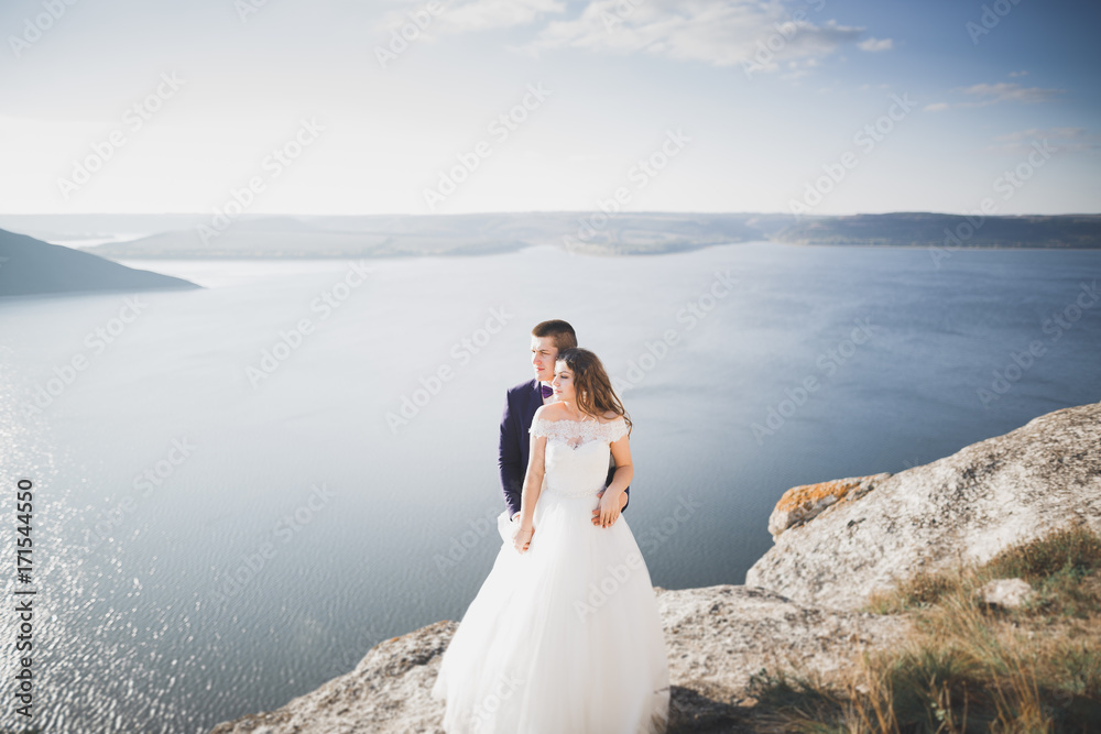 Wedding couple kissing and hugging on rocks near blue sea Wedding couple kissing and hugging on rocks near blue sea