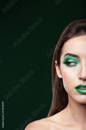 Young woman with bright green makeup on black background