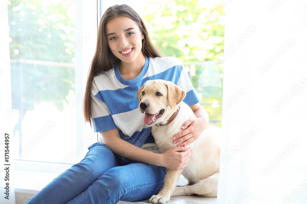 Young woman sitting with yellow retriever near window