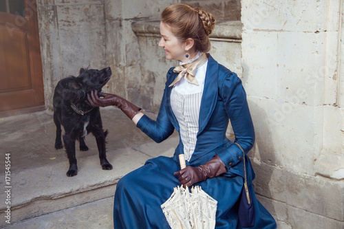 Vintage young beautiful lady with black dog outdoors. Victorian style