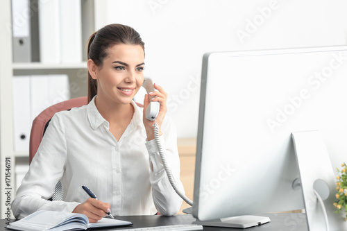 Young female receptionist talking on phone in office