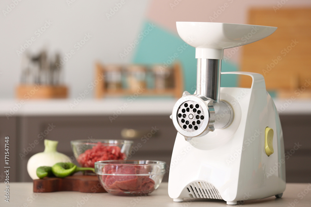 Foto Meat grinder with fresh meat on kitchen table