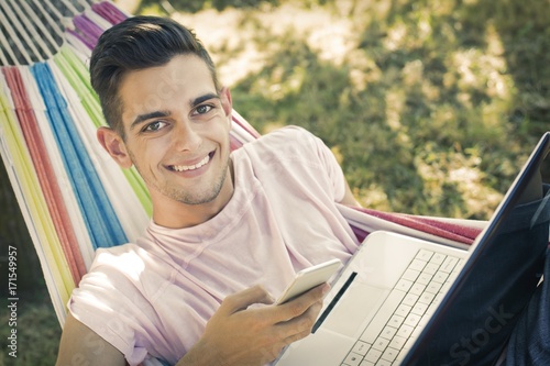 young man or teenager with the laptop in the hammock at sunset summer