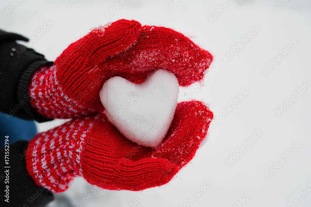 red female gloves hold a white heart from the snow