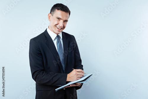 Joyful mature man noting something in notebook