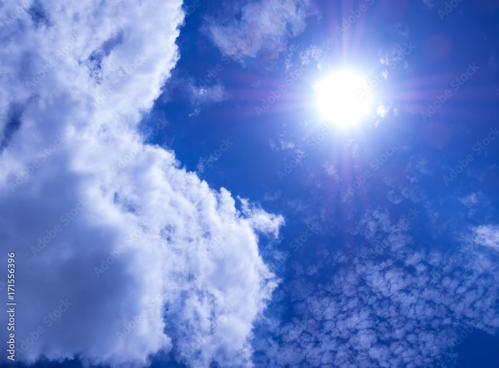 White fluffy clouds in the bright blue sky with light from the Sun