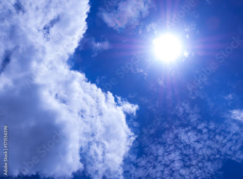 White fluffy clouds in the bright blue sky with light from the Sun
