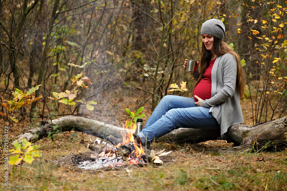 Beautiful pregnant woman rests in the forest. She sits near the fire, and drink tea. The concept of family happiness
Beautiful pregnant woman rests in the forest. She sits near the fire, and drink tea. The concept of family happiness