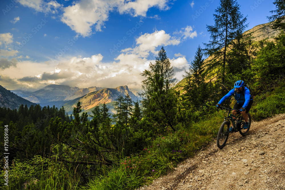 Fototapeta premium Tourist cycling in Cortina d'Ampezzo, stunning rocky mountains on the background. Man riding MTB enduro flow trail. South Tyrol province of Italy, Dolomites.