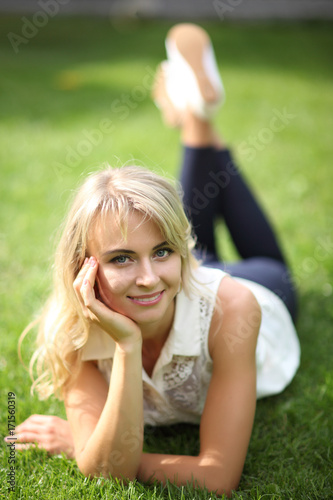 Beautiful young long-haired blonde posing for camera lying on grass. Young beautiful blond flirting with the camera. Blonde lying on green grass and looking at camera