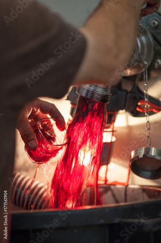 Winemaker holds glass under stream of wine from faucet photo