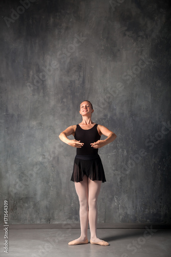 Young beautiful ballerina in a black dress, pointe shoes standing in a dance position in front of a ballet in a dark dance studio