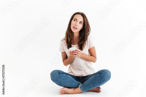 Pensive brunette woman using smartphone and looking up