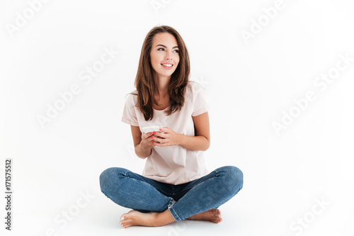 Pleased brunette woman sitting on the floor with smartphone