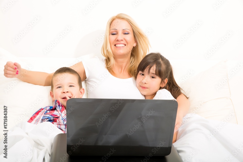 Mother with her kids using a laptop in bed