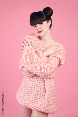 Fashion studio teen look style over pink. Fashionable young girl wears wool knitting sweater. Brunette with matte lips and bun hairstyle in soft pullover posing isolated on studio background. photo