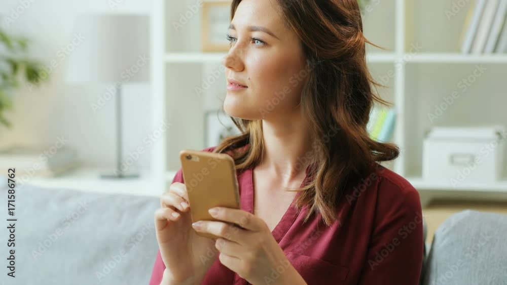 Portrait of attractive young woman using her smartphone while sitting on the sofa at home in the living room. Portrait of attractive young woman using her smartphone while sitting on the sofa at home in the living room.