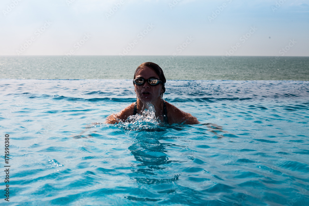Girl in glasses in a swimming pool with sea view