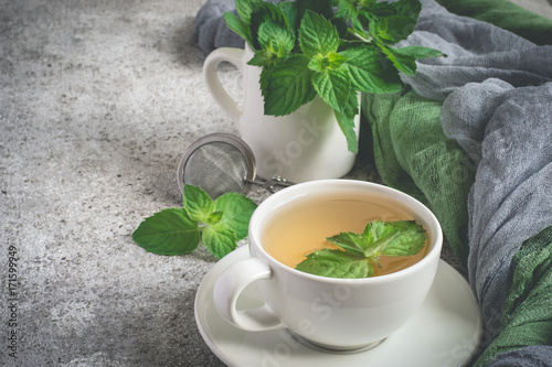 Natural mint tea and fresh mint leaves on a gray background