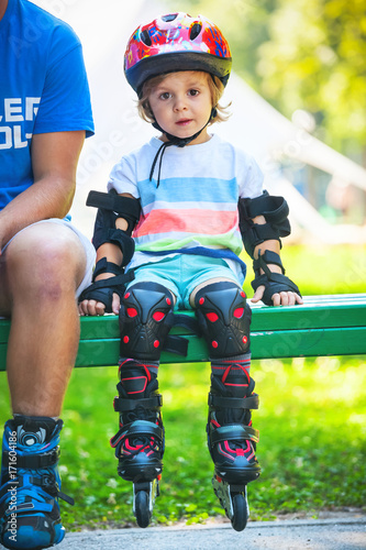 Portait of cute baby boy with inline skates sitting on bench.