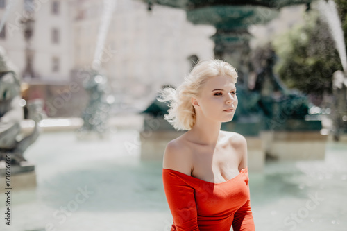 Close-up portrait of a blond girl with blonde hair posing in park on fountain background.