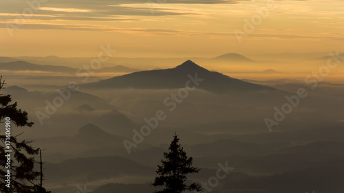 Strong orange sunset over hills hidden under fog.