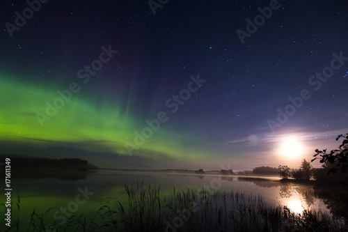 Aurora borealis and full moon rich colors above lake in Finland