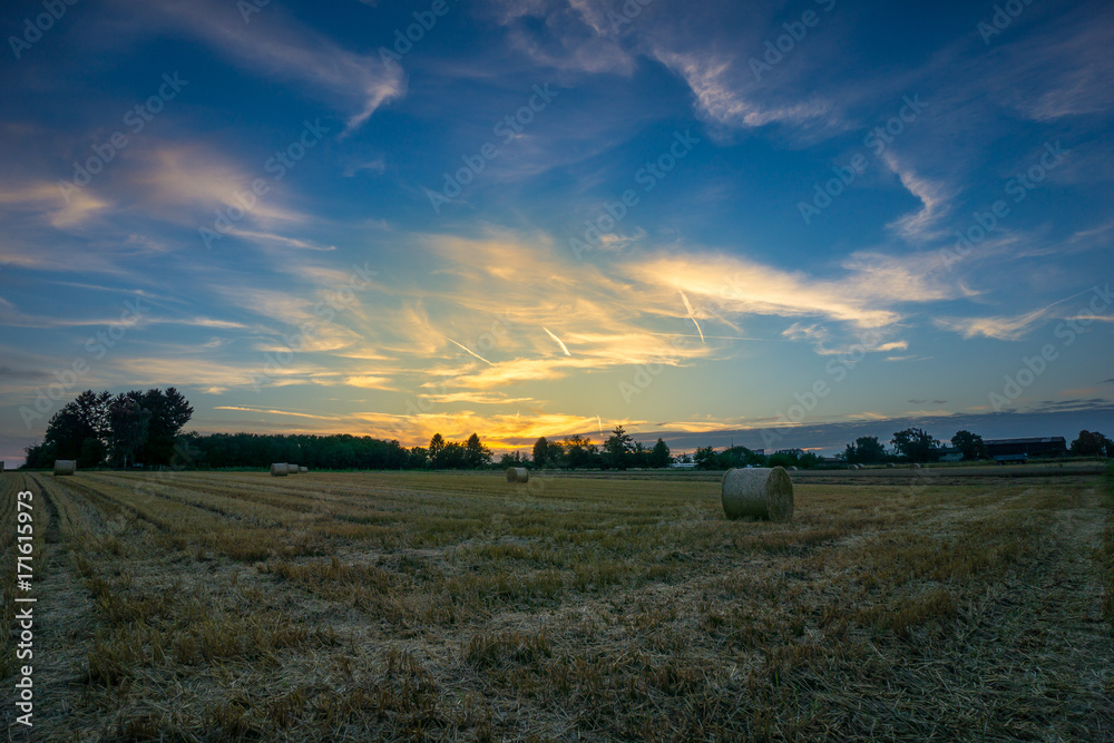Beautiful colorful orange sunset over field with hay bales and blue sky