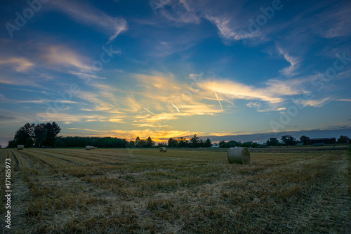 Beautiful colorful orange sunset over field with hay bales and blue sky
