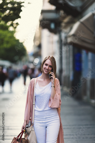 Beautiful and fashionable young woman with shopping bags standing on city street and looking at shopfront