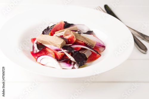Salad with tuna, sweet onion, fresh tomato in a white plate on a white wooden background, horizontal, selective focus 