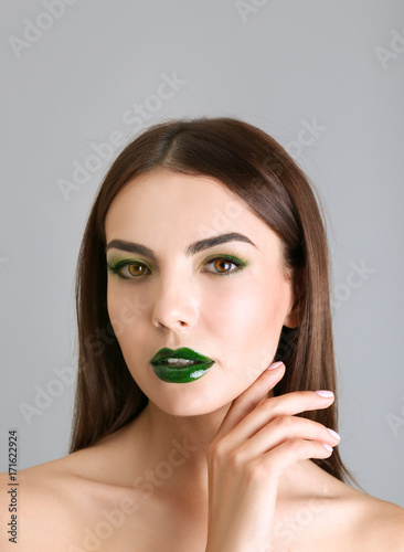 Young beautiful woman with fancy green makeup on color background