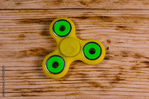 Yellow fidget spinner on wooden desk. Top view
