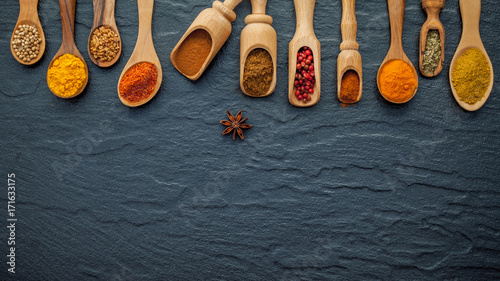 Fototapeta Naklejka Na Ścianę i Meble -  Various of Indian spices and herbs in wooden spoons. Flat lay of spices ingredients chilli ,pepper, garlic,dries thyme, cinnamon and star anise on the black stone.