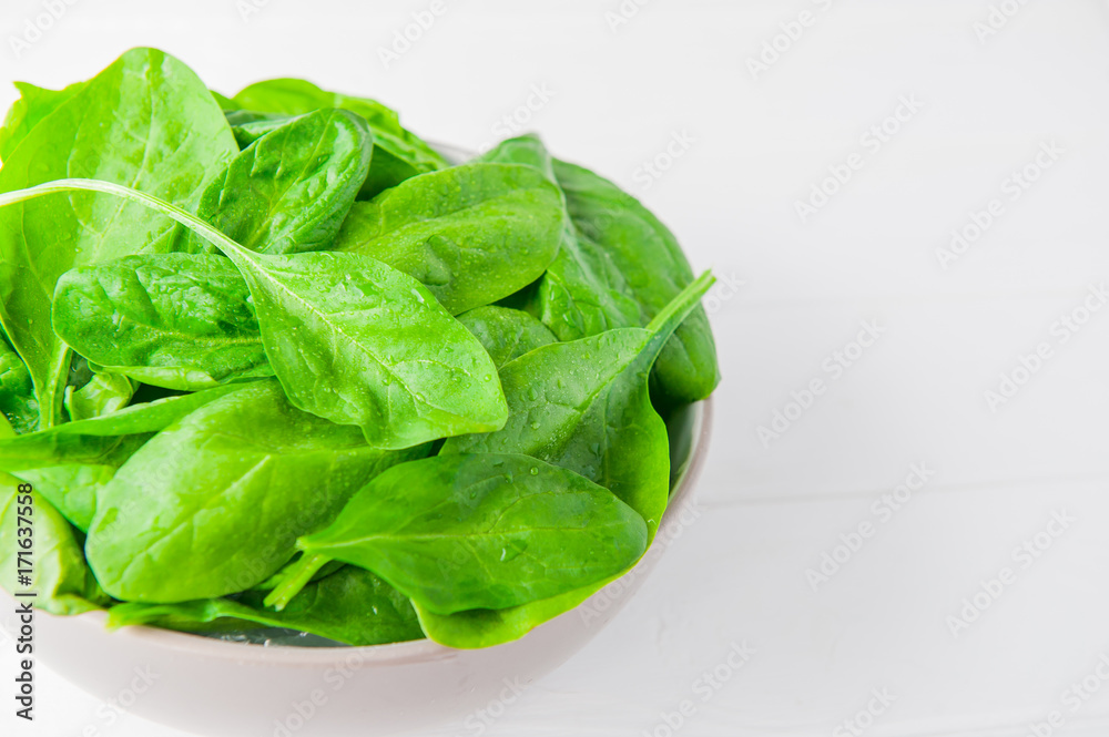 Fresh spinach leaves with water drops in ceramic bowl on thw white wooden background. Selective focus. Space for text Fresh spinach leaves with water drops in ceramic bowl on thw white wooden background. Selective focus. Space for text