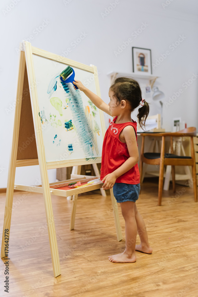 Cute little girl painting at home using an easel stand Cute little girl painting at home using an easel stand