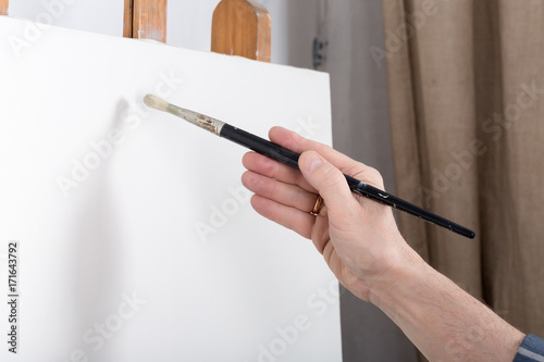 An artist in studio thinking in front of white canvas
