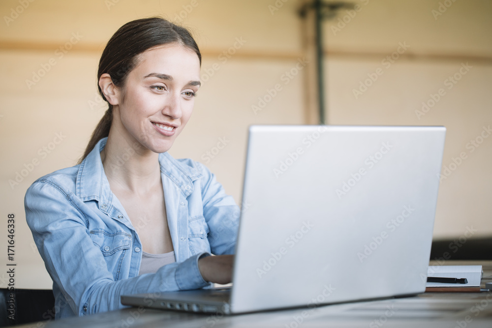Smiling young woman typing on laptop at table Smiling young woman typing on laptop at table