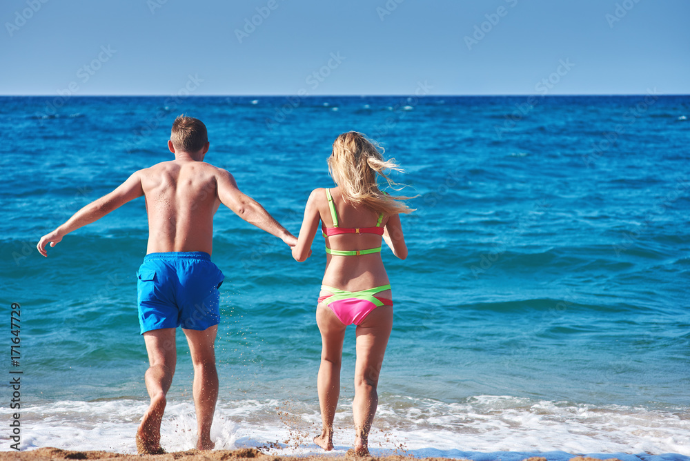 Caucasian couple running into the sea water. Back view.