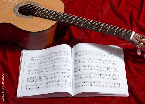 acoustic guitar and music notes on red velvet fabric, close view of objects