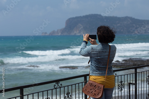 Woman taking mobile photo of sea and rocks 